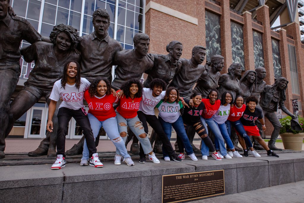 Members of NPHC fraternities and sororities standing in front of the War Hymn Statue, leaning to the right in unison